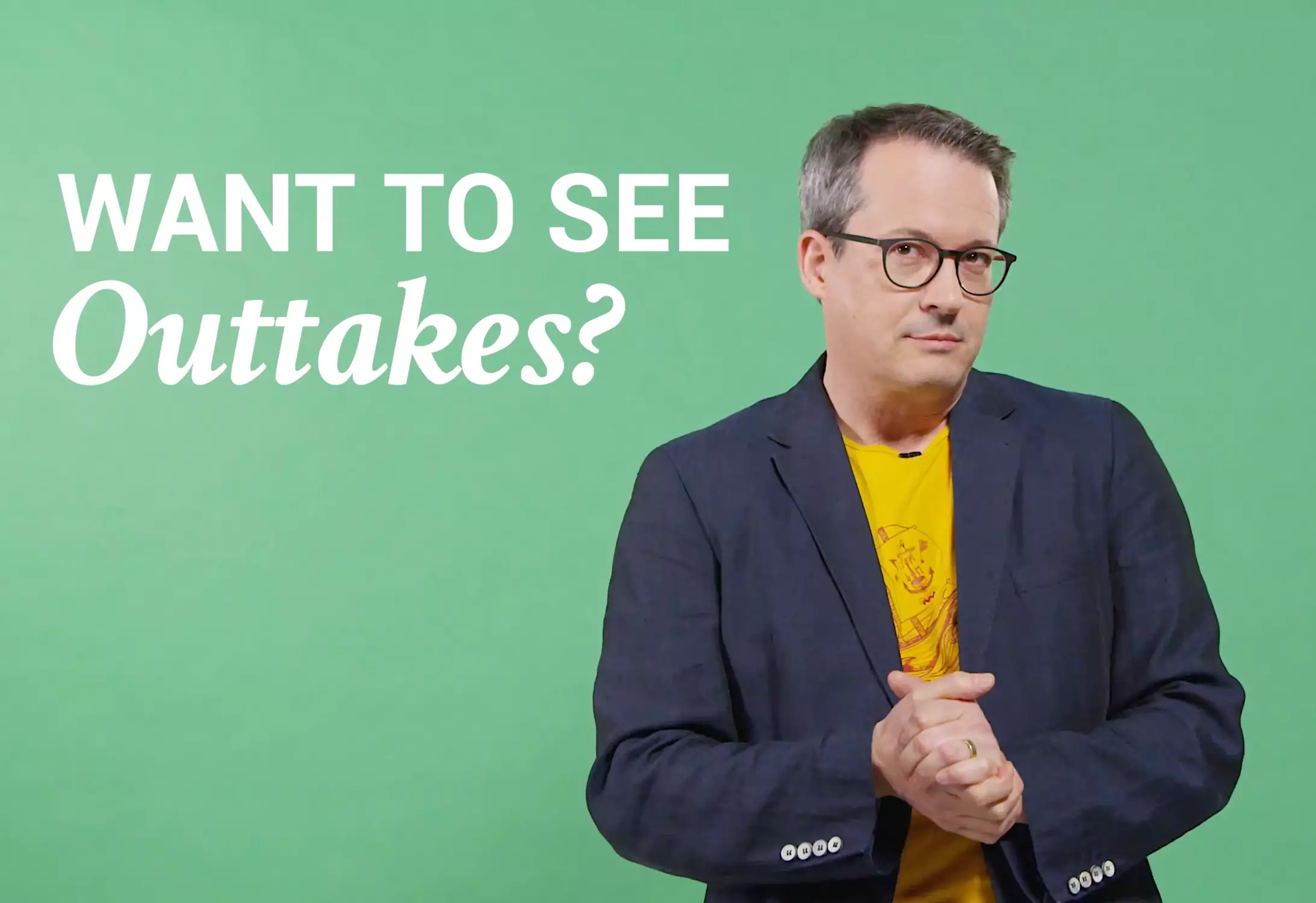 Stefan Hilß looking questioningly in a yellow shirt and dark jacket in front of a light green wall.